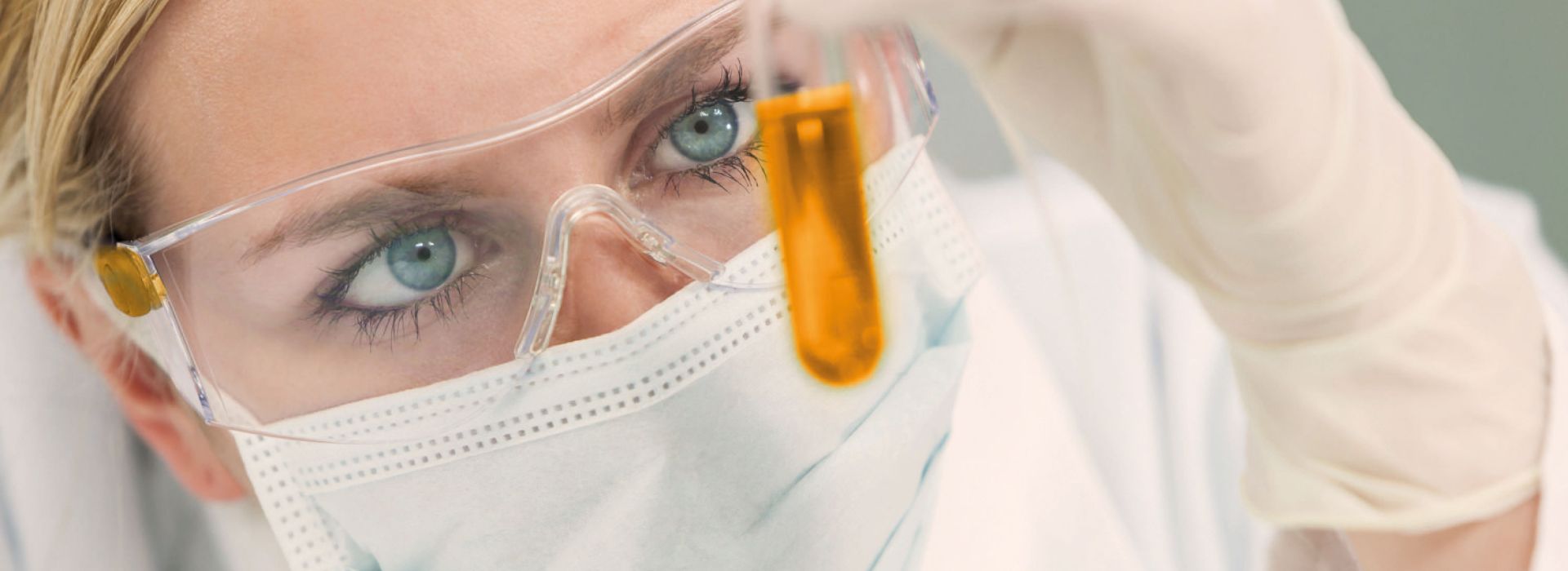 Ärztin mit Gesichtsmaske und Schutzbrille hält Reagenzglas mit Flüssigkeit in der Hand