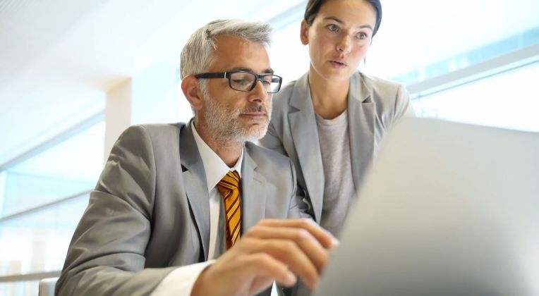 Business Intelligence Lösugen für Kommunen und Verwaltungseinrichtungen mit AKQUINET. Ein Mann und eine Frau in Business Kleidung vor einem Laptop.