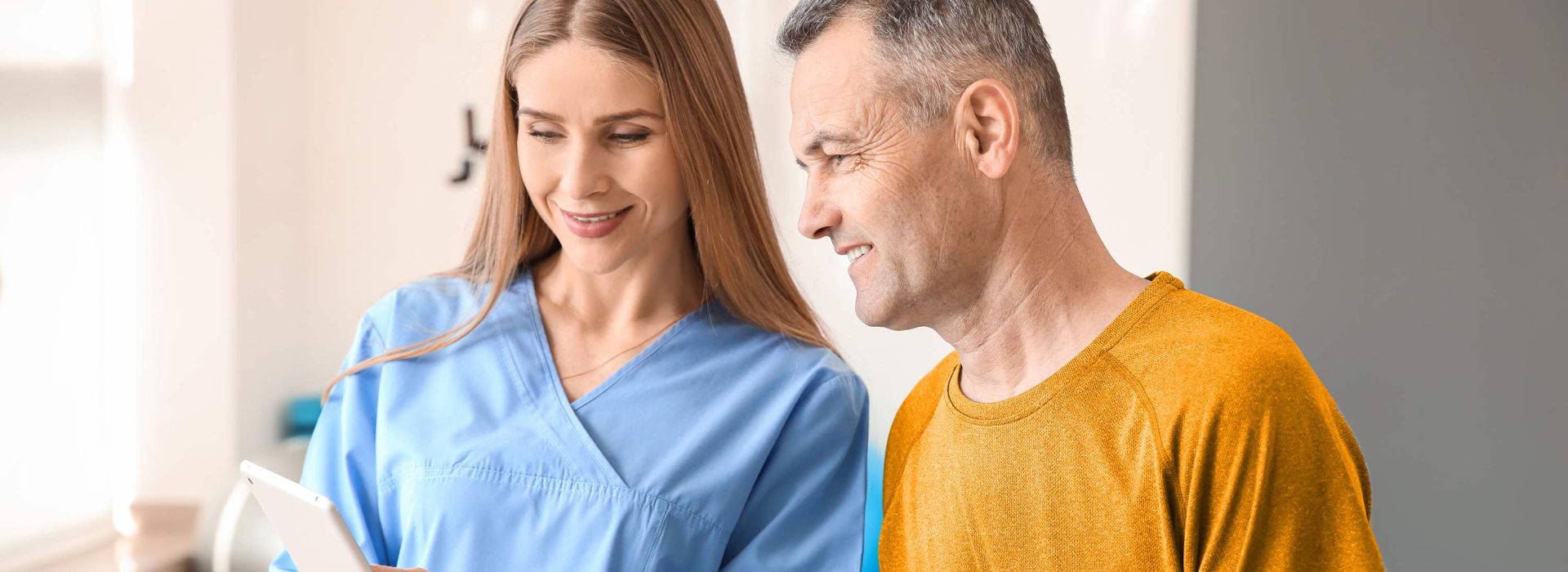 Eine gut gelaunte, junge Ärztin zeigt einem gut gelaunten Patienten medizinische Informationen auf ihrem Tablet