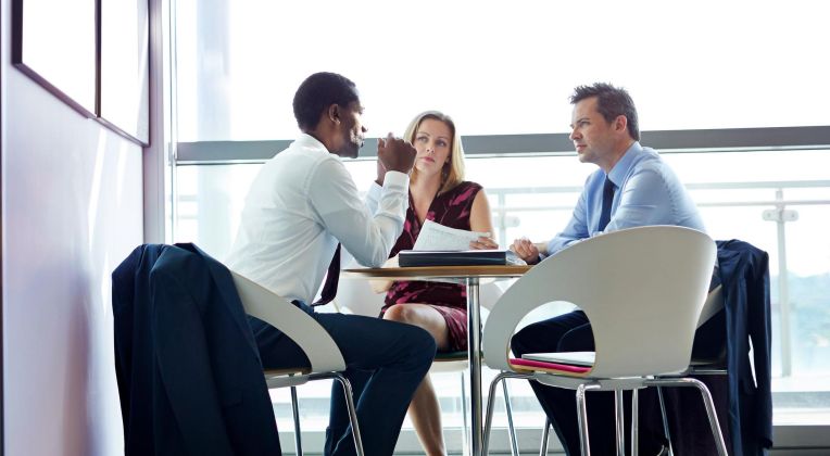 Drei Personen in Businesskleidung sitzen zusammen an einem Tisch.