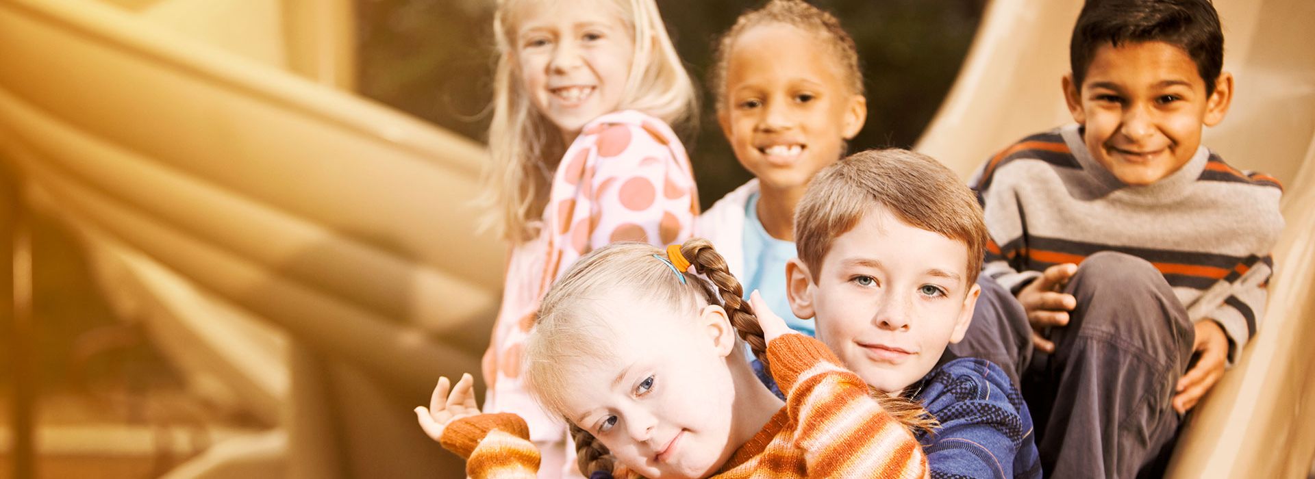Eine freundliche Gruppe von Kindern ist zu sehen wie sie zusammen auf einer Rutsche sitzen und in die Kamera gucken.