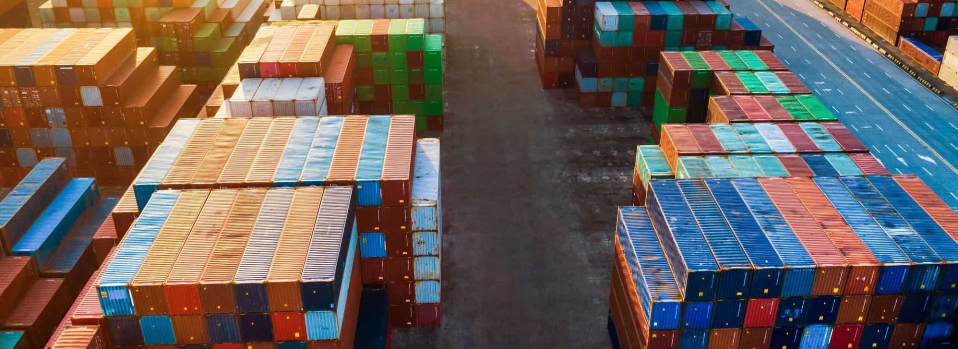 Stacks of containers as far as the eye can see. A three-lane road on the right. Mountains in the background.
