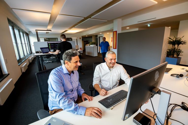 Mitarbeitende von AKQUINET tauschen sich aus und sitzen dabei vor einem Computer.