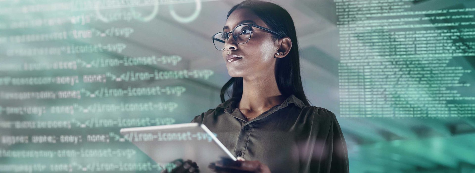 A woman with a tablet in her hand looks at IT code lines