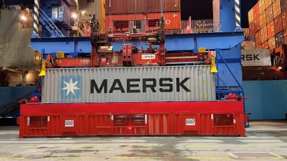 A container labeled "Maersk" is lifted into the air by a crane at a port terminal.