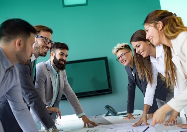 A team of colleagues stands together at a conference table.