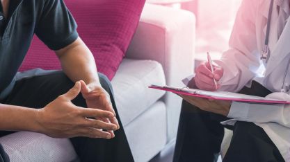 Man sieht die Hände von zwei Männern im Gespräch, einer schreibt etwas auf einen Schreibblock.