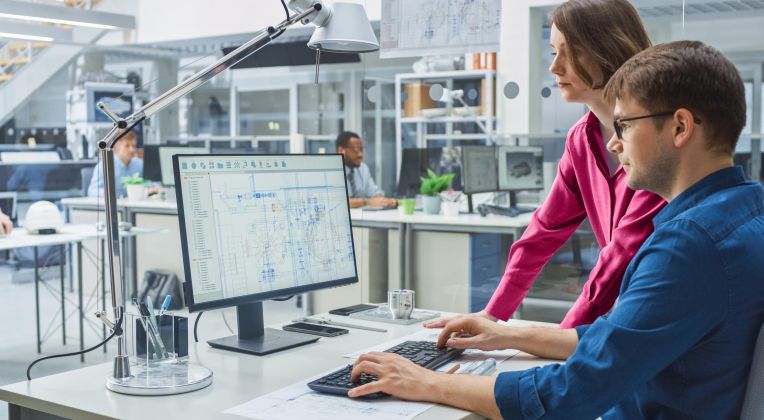 Zwei Personen siezten von einem Monitor und schauen gemeinsam darauf.