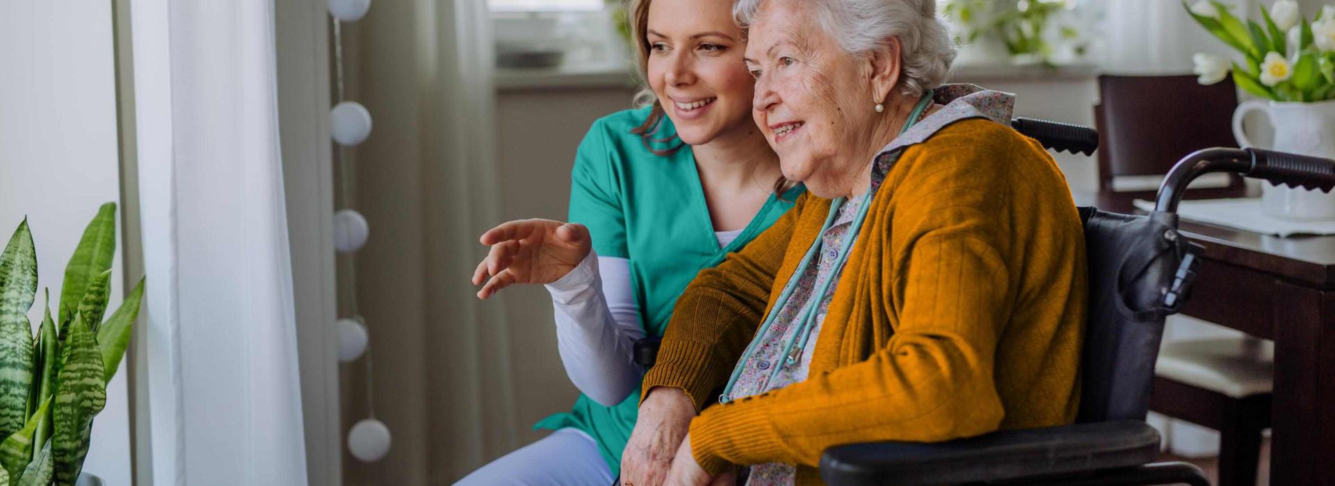 Krankenschwester und ihr älterer Kunde im Rollstuhl schauen aus dem Fenster