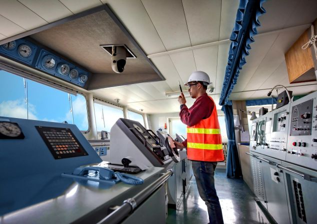 Eine Person in Sicherheitsweste steht auf der Brücke eines Schiffes.