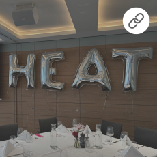 Silberne Luftballons, die das Wort HEAT bilden fliegen neben einem gedeckten Tisch.