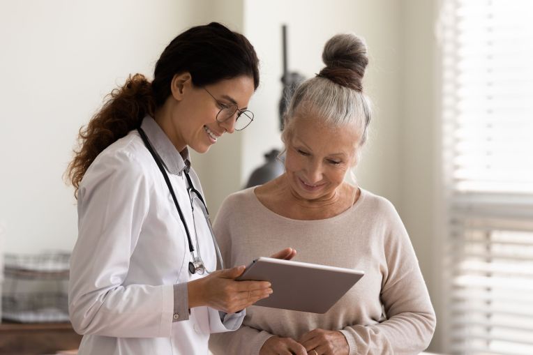 Eine Ärztin zeigt ihrer älteren Patientin etwas auf einem Tablet