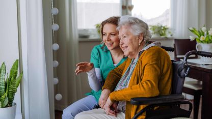 Krankenschwester und ihr älterer Kunde im Rollstuhl schauen aus dem Fenster
