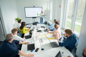 Power BI Schulungsteilnehmer sitzen mit Laptops am Tisch, der Trainer zeigt etwas am Flipchart