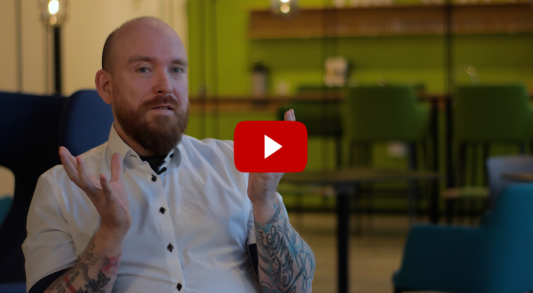 Marcus im AKQUINET Haus während der Drehaufnahmen zu Datenmanagement. Im Vordergrund ist ein YouTube-Symbol zu sehen.