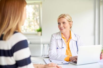 Ärztin sitzt am Schreibtisch vor einem Laptop und ist im Gespräch mit einer Patienten