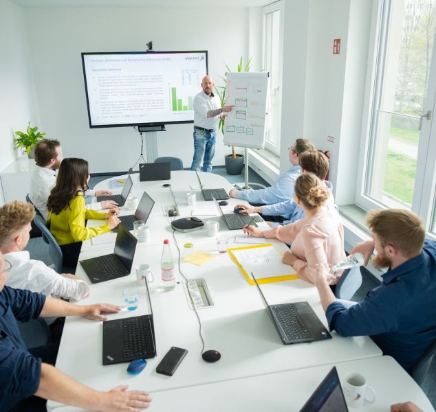 Power BI Schulungsteilnehmer sitzen mit Laptops am Tisch, der Trainer zeigt etwas am Flipchart