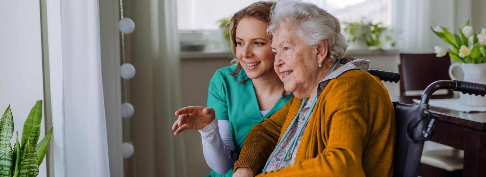 Krankenschwester und ihr älterer Kunde im Rollstuhl schauen aus dem Fenster