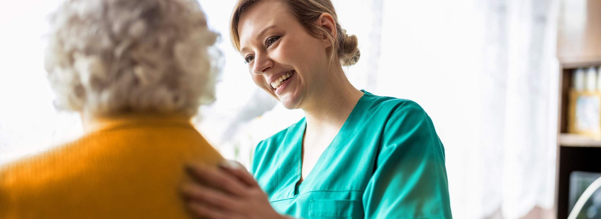 Pflegerin besucht alte Patientin zu Hause und legt ihre Hand auf den Rücken