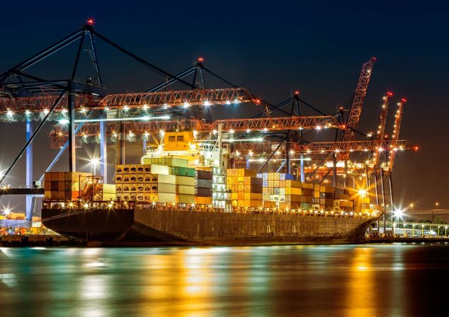 Beleuchteter Hafenterminal bei Nacht mit Containerschiff und Kränen.