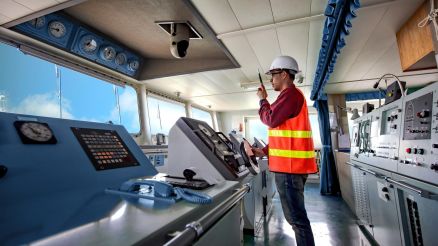 Eine Person in Sicherheitsweste steht auf der Brücke eines Schiffes.