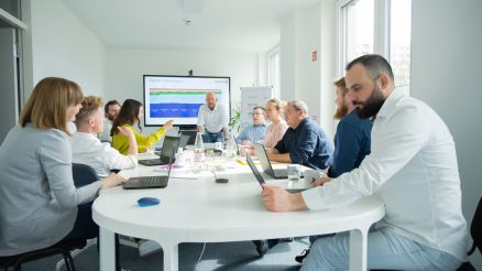 MS Fabric Schulungsgruppe an einem Tisch mit Laptops und einem Trainer am Tischende.