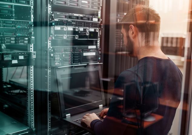 A man sits at a rack checking data on a notebook.