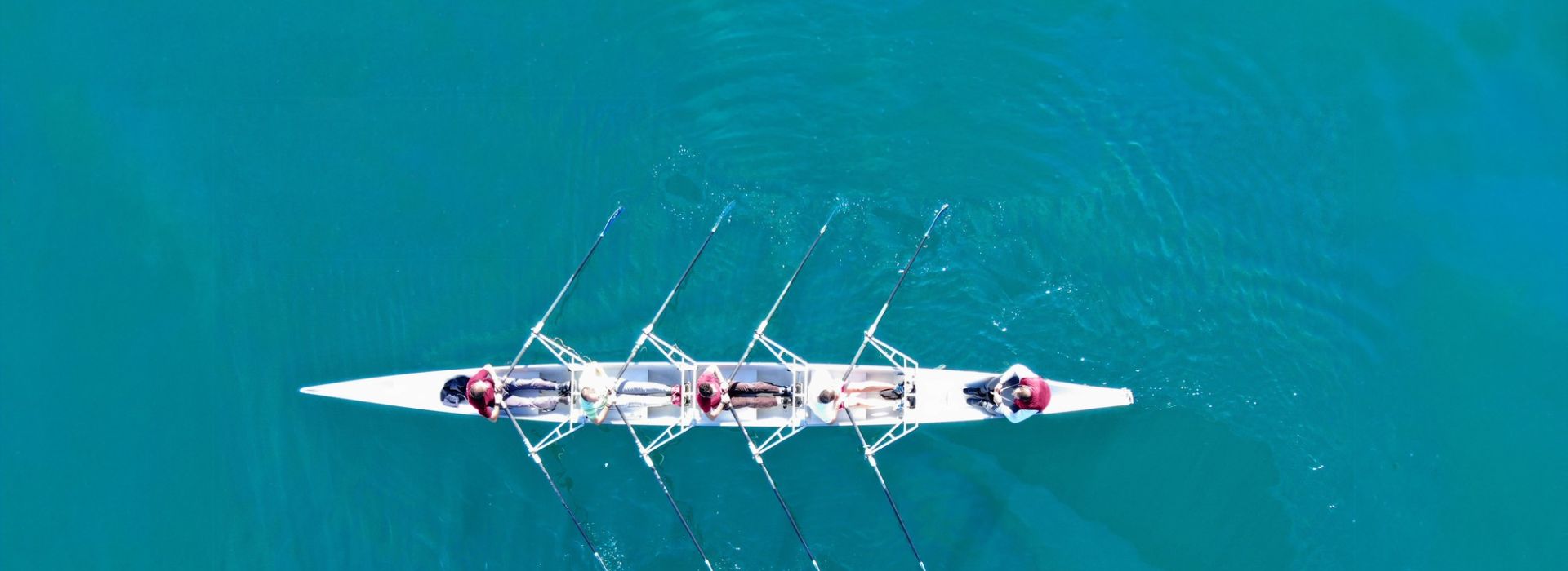 Bird's eye view of a four-man rowing boat on a turquoise water.