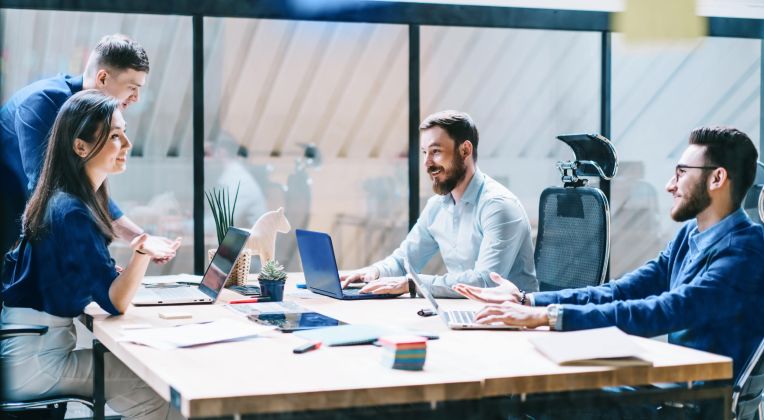 Ein Team von Kolleg*innen sitzt gemeinsam an einem Arbeitsplatz und diskutiert Themen.