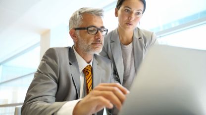 A man and a woman in business attire in front of a laptop.