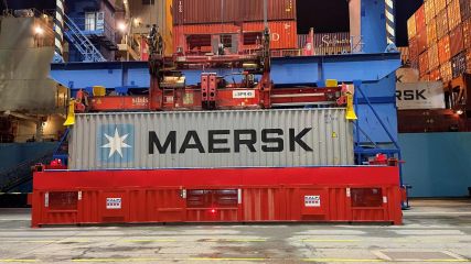 Ein Container mit der Aufschrift "Maersk" wird von einem Kran auf einem Hafenterminal in die Luft gehoben.