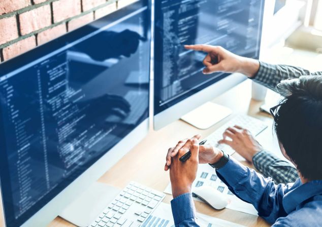 Zwei Entwickler betrachten den Code für die AKQUINET 365 Branchen Cloud auf zwei Monitoren.