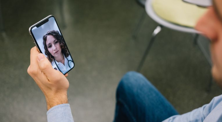 Ein Mann bespricht über kvvideo von AKQUINET seine Erkältungssymptome mit seiner Ärztin über ein Videocall auf dem Smartphone