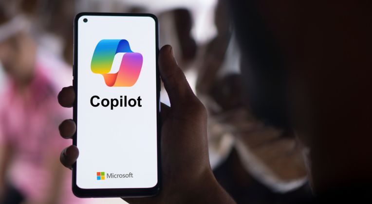 Eine Hand hält ein Smartphone mit dem Microsoft Copilot Logo. Microsoft Fabric sorgt dafür, dass Ihre Unternehmensdaten jederzeit zugänglich und aktuell sind, sodass Copilot speziell auf Ihr Unternehmen zugeschnittene Analysen und Berichte erstellen kann.