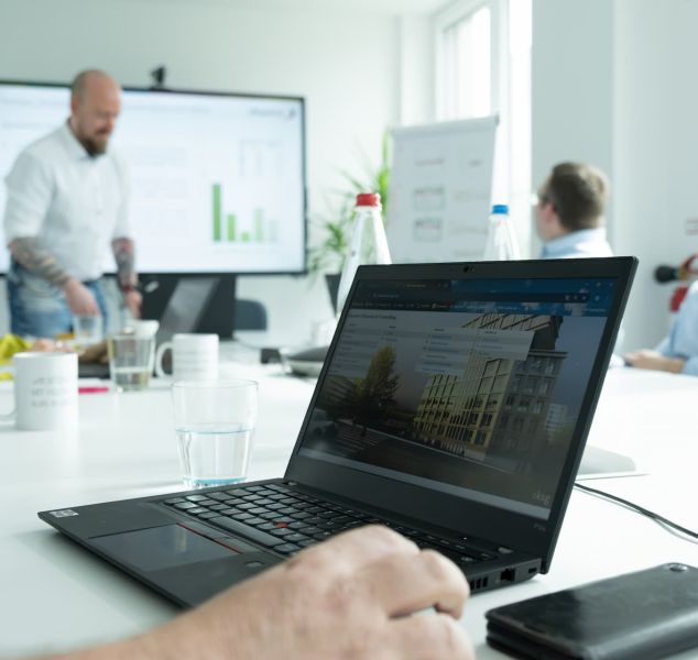 Schulung am Tisch, im Vordergrund ein offener Laptop, ein Trainer am Smartboard.