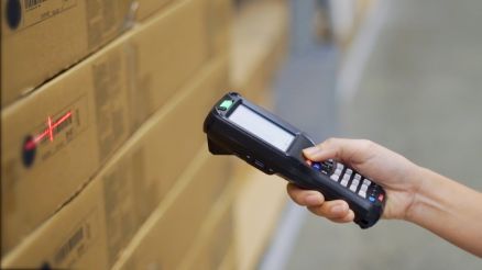 Hand mit einer Scanner-Lösung, die einen Barcode auf einem Paket einscannt