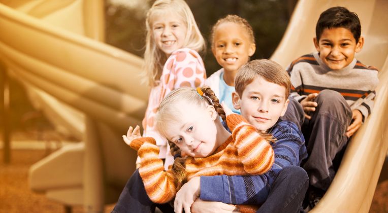 Eine freundliche Gruppe von Kindern ist zu sehen wie sie zusammen auf einer Rutsche sitzen und in die Kamera gucken.