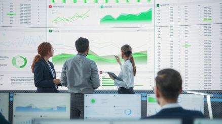 Drei Personen stehen vor großen Bildschirmen mit Datenvisualisierungen und Diagrammen, die Datenqualität und Governance symbolisieren.