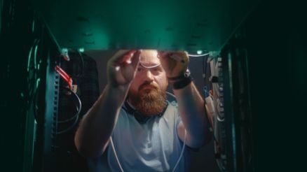 Ein Mann mit blauem Hemd und Bart verkabelt einen Server in einem Rack