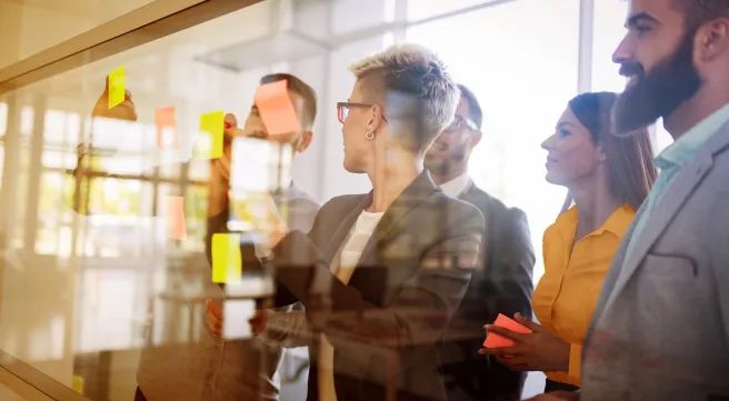 Einige Personen stehen an einem transparenten Board und beraten sich.