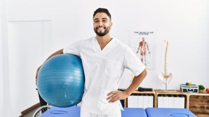 Ein Physiotherapeut hält einen Gymnastikball in der Hand und lächelt in die Kamera