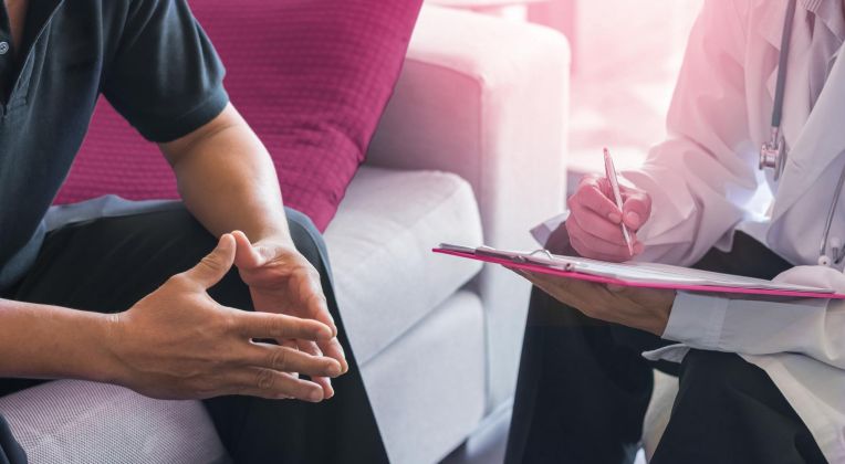 Man sieht die Hände von zwei Männern im Gespräch, einer schreibt etwas auf einen Schreibblock.