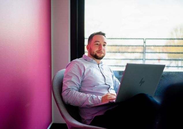 Eine männliche Person sitzt mit einem Laptop in einem Sessel und arbeitet.