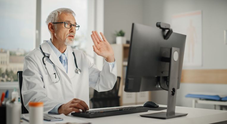 Ein ältere Arzt nutzt kvvideo von AKQUINET um einem Patienten einen unauffälligen Labor-Befund mitzuteilen