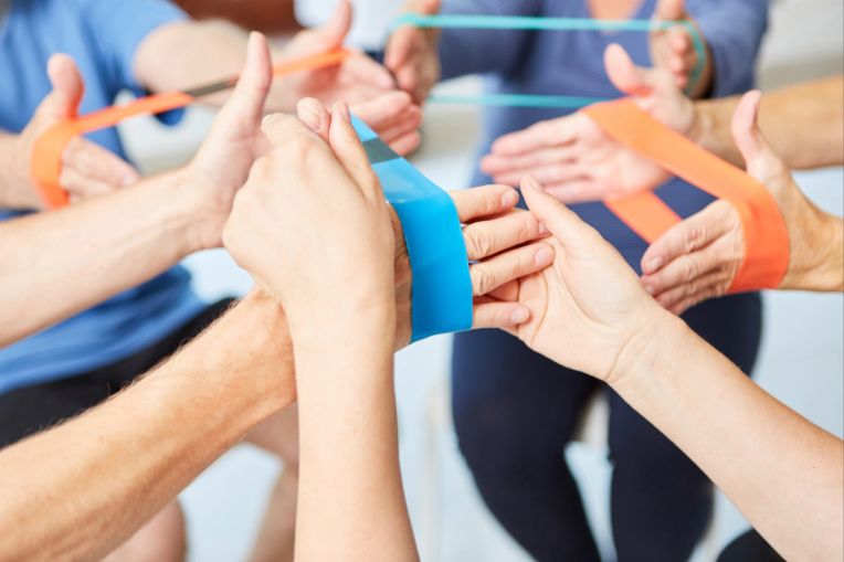 Eine Ergotherapie-Stunde in der ältere Menschen mit Gymnastikbändern trainieren