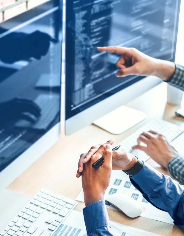 Zwei Entwickler betrachten den Code für die AKQUINET 365 Branchen Cloud auf zwei Monitoren.