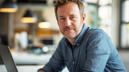 Ein Mann sitzt am Schreitisch und schaut in die Kamera.