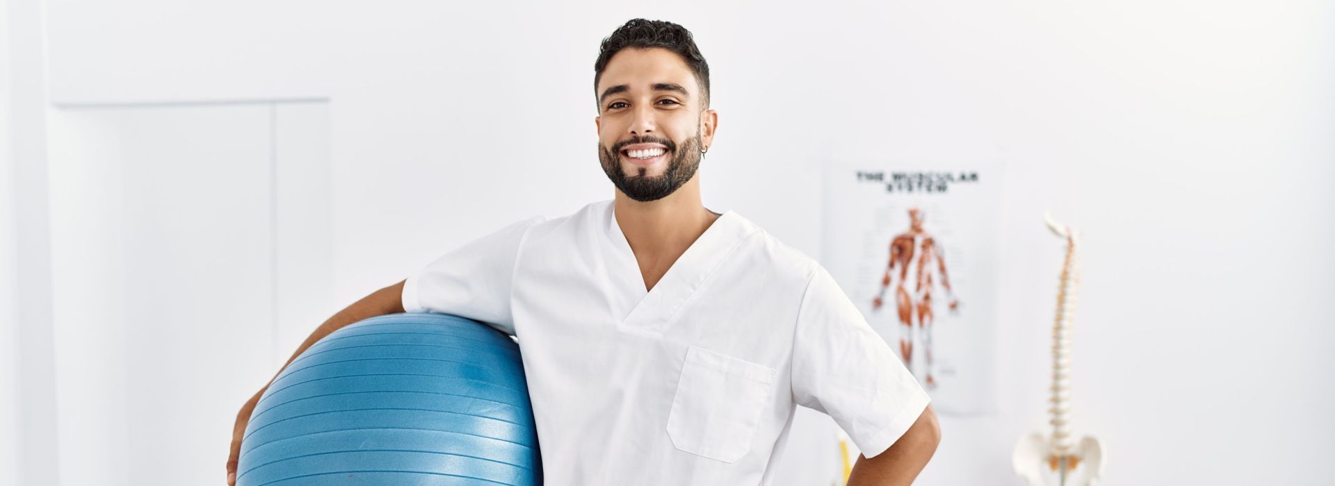 Ein Physiotherapeut hält einen Gymnastikball in der Hand und lächelt in die Kamera