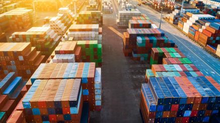 Containerstapel so weit das Auge reicht. Rechts eine dreispurige Straße. Berge im Hintergrund.