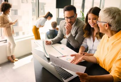 A business team looks at analysis results om a laptop and charts.
